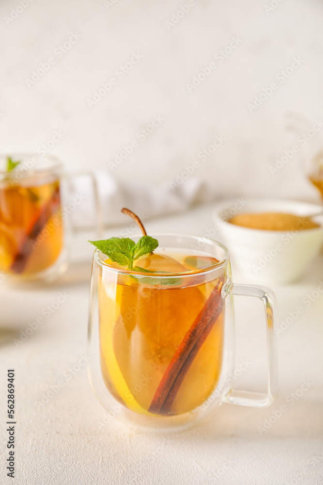 Glass cup of fruit tea with pear, mint and cinnamon on light background, closeup