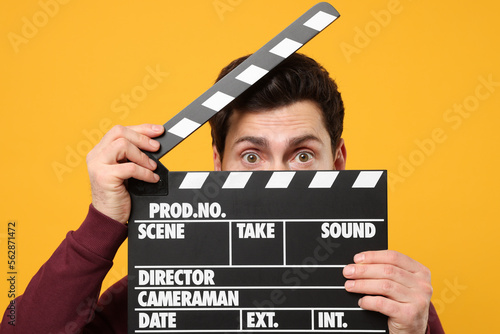 Obraz na płótnie Surprised actor holding clapperboard on orange background