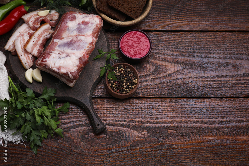 Pieces of pork fatback served with sauce and spices on wooden table, flat lay. Space for text