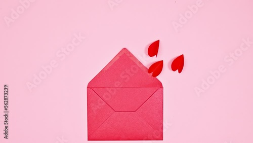 Flying hearts with wings enter in red envelope on pastel pink background. Flat lay. Stop motion