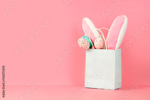 Fotobehang Easter bunny ears and eggs in a paper bag on pink background with copy space