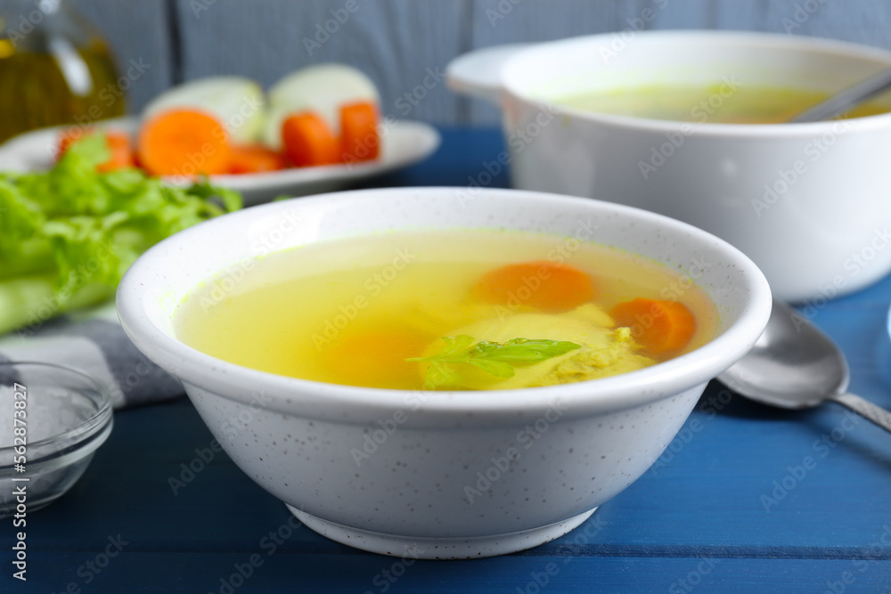 Delicious chicken bouillon with carrot and celery on blue wooden table, closeup Delicious chicken bouillon with carrot and celery on blue wooden table, closeup