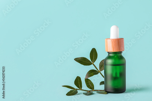 Bottle of serum and plant leaves on color background
