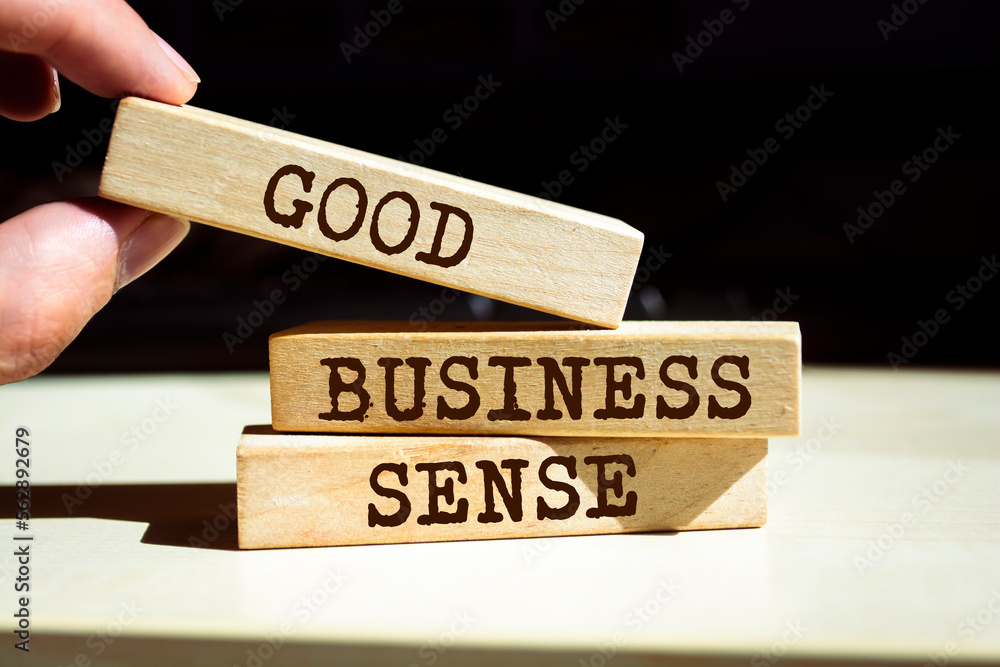 Closeup on businessman holding a wooden blocks with text 'GOOD BUSINESS SENSE', business concept Closeup on businessman holding a wooden blocks with text 'GOOD BUSINESS SENSE', business concept