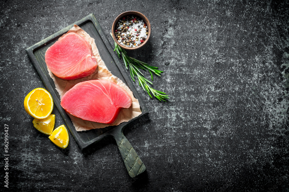 Fresh raw tuna steak on a cutting Board with lemon slices, rosemary and spices. Fresh raw tuna steak on a cutting Board with lemon slices, rosemary and spices.