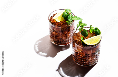 Photography Rum cola cocktail with strong alcohol and ice, garnished with mint and lime in glass