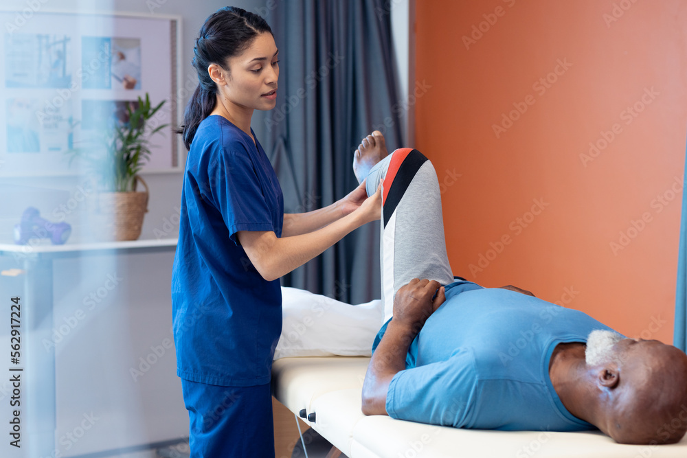 Obraz premium Diverse female physiotherapist treating leg of senior male patient in therapy, copy space