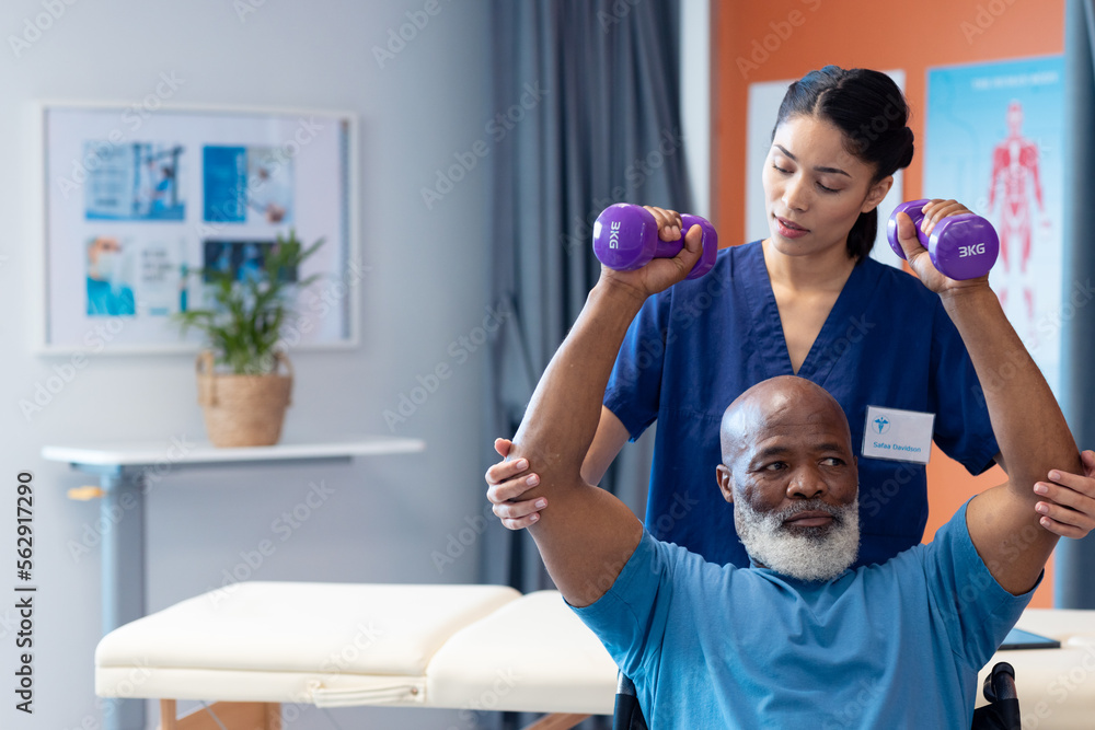 Obraz premium Diverse female physiotherapist helping senior male patient exercise with dumbbells, copy space