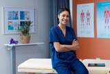 Portrait of biracial female physiotherapist smiling in hospital therapy room, copy space