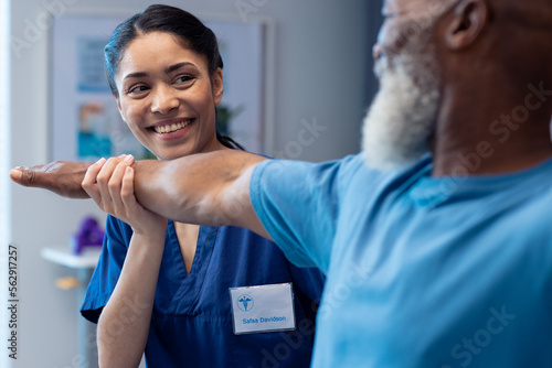 Smiling diverse female physiotherapist treating arm of senior male patient, copy space