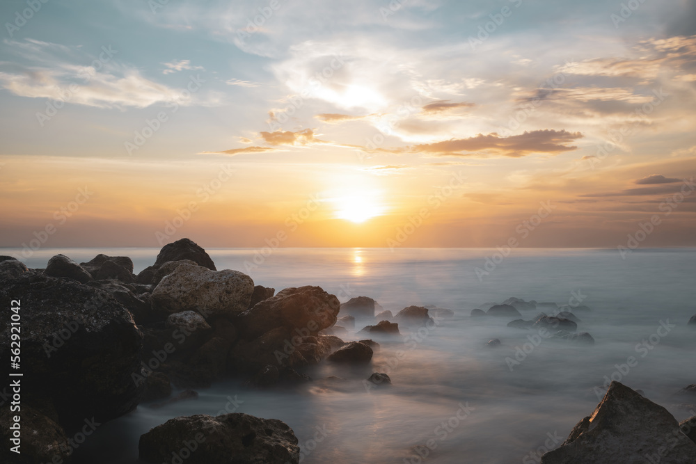 (Long exposure) Stunning seascape with some rocks in the foreground and the sun setting in the distance. Lombok Island, West Nusa Tenggara, Indonesia.