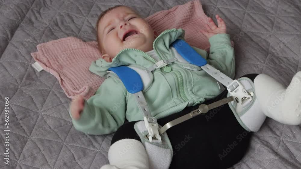 Baby girl in Pavlik Harness to correct Hip Dysplasia cries while lying