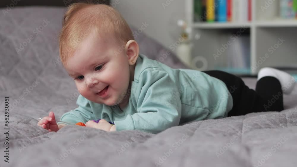 Smiling, happy baby girl on blanket lying on her tummy plays with chewing toy Smiling, happy baby girl on blanket lying on her tummy plays with chewing toy