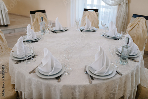 Festive chairs and table decorated and serving cutlery for guests covered with a tablecloth, served to stand in the wedding banquet hall.