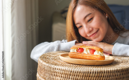 Portrait image of a woman holding and looking at a plate of strawberry Eclair