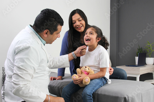 Latina mother cares for and accompanies her curly little daughter at the dark-haired pediatrician specialist doctor's office to prevent abuse and harassment at her medical checkup
