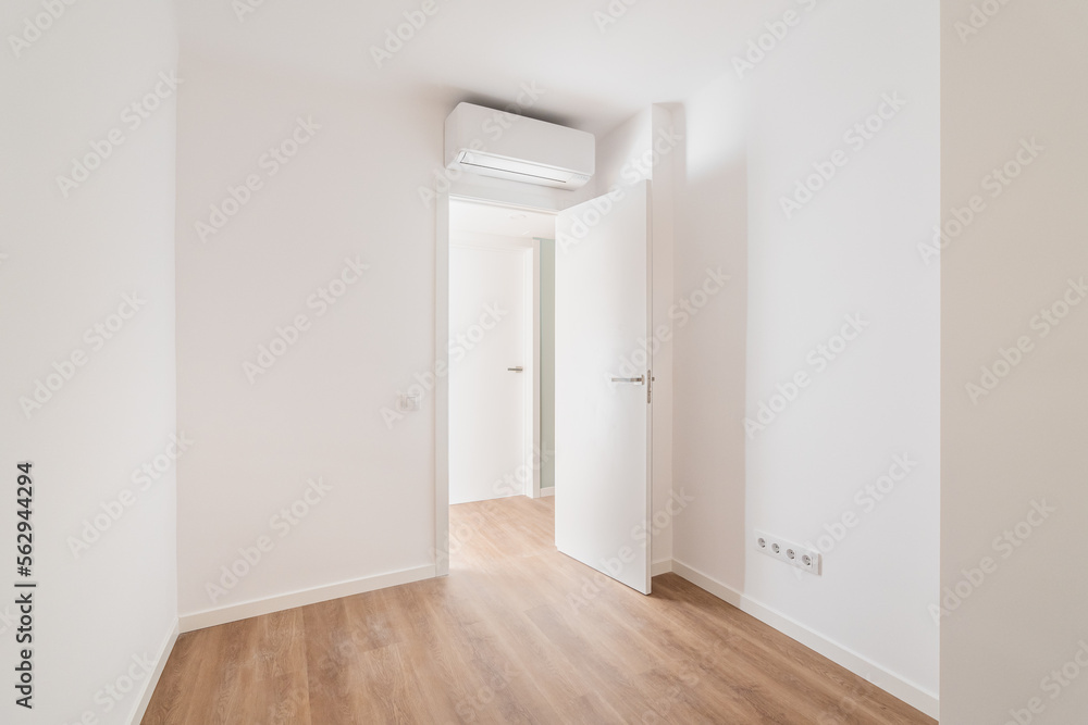 Empty bedroom with parquet flooring. An open door from the room leading to a corridor with other rooms. Air conditioning above the door saves from summer heat