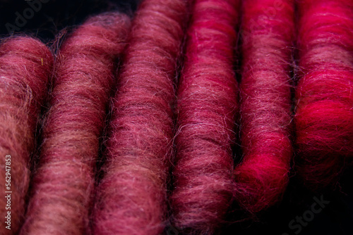 Six merino wool rolags arranged next to each other on a black background, with colours ranging from coral to pink and red.