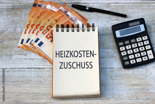 Das Wort Heizkosten Zuschuss ist auf einem Notizblock mit Taschenrechner und Euro-Banknoten abgebildet.