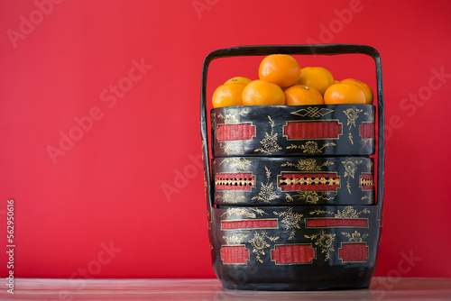 Mandarin oranges are in a tiffin or basket called Bakul Siah, traditional Peranakan Baba Malay art. The concept of auspicious ceremonies, Chinese New Year, and weddings. Isolated on a red background. photo