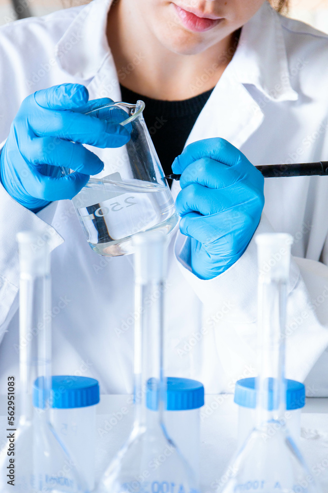 Fototapeta premium Close up left handed woman scientist labeling beaker samples with blue gloves and equipment. Lab technician writing. Development and research. No face.