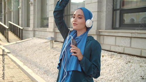 Middle eastern woman in hijab listening music with headphones and dancing. Woman independence and feminism concept. photo