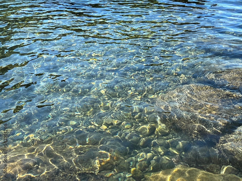 Sea crystal clear healing water with smooth stones and pebbles at the bottom.