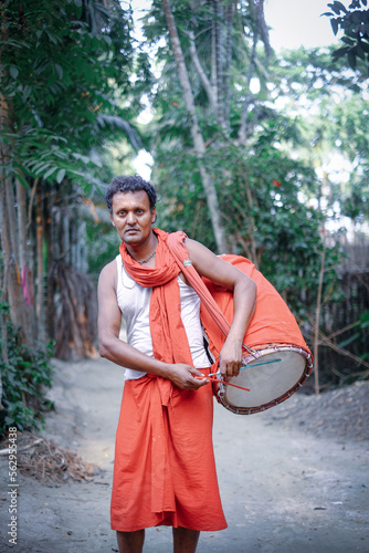 Hindu religious middle aged man playing traditional musical instrument named dhak in village outdoor wearing a gerua dress specially made for monks  photo