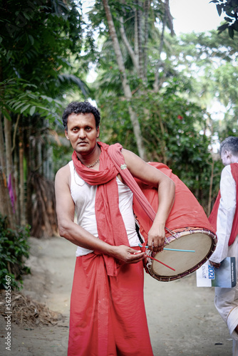 Hindu religious middle aged man playing traditional musical instrument named dhak in village outdoor wearing a gerua dress specially made for monks  photo