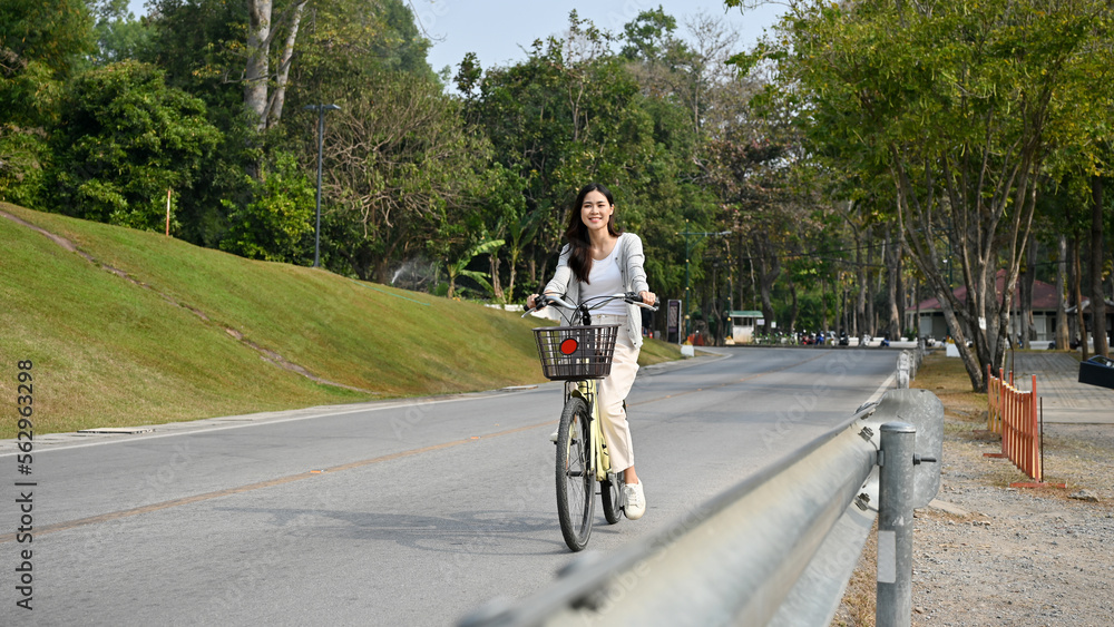 Happy and chill young Asian woman riding a bicycle on the road in public park