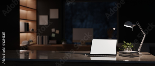 Modern office at night with tablet mockup on table over blurred dark office room in background. photo