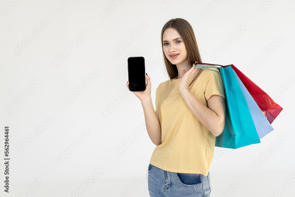 Naklejka premium Happy woman standing with satisfied look showing shopping bags and smart phone with blank screen for advertisement isolated on white background.