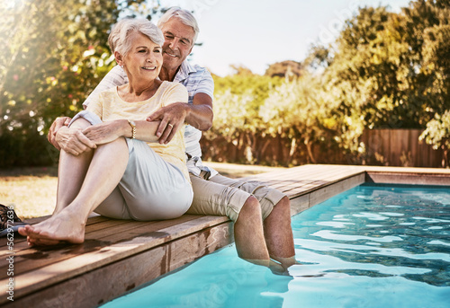 Senior couple, hug and relax by pool for love and summer vacation, bonding or quality time together in the outdoors. Happy elderly man and woman relaxing and hugging with feet in water by a poolside