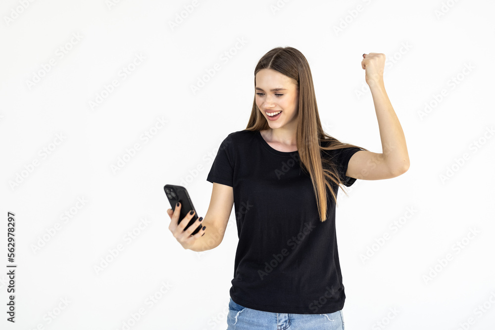 Young woman winning on mobile phone, rejoicing and screaming of joy while using smartphone app, standing over white background Young woman winning on mobile phone, rejoicing and screaming of joy while using smartphone app, standing over white background