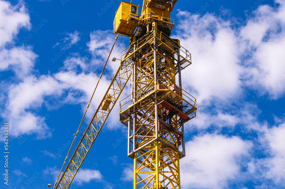 Construction of buildings using a tower crane. Construction equipment. Tower crane and blue sky clouds. Lifting of building structures and materials to a height using a tower crane. Construction of buildings using a tower crane. Construction equipment. Tower crane and blue sky clouds. Lifting of building structures and materials to a height using a tower crane.
