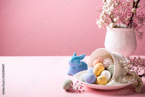 Easter composition with spring flowers and colorful quail eggs in porcelain white coffee cup over pink background. Springtime and Easter holiday concept with copy space