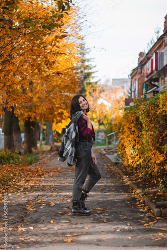 Autumn portrait of an attractive young woman on a city street with yellow tree leaves, outdoors