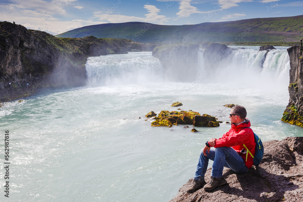 Man in red jacket looking at Godafoss waterfall. Beautiful landscape in Iceland