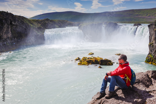 Man in red jacket looking at Godafoss waterfall. Beautiful landscape in Iceland © olyphotostories