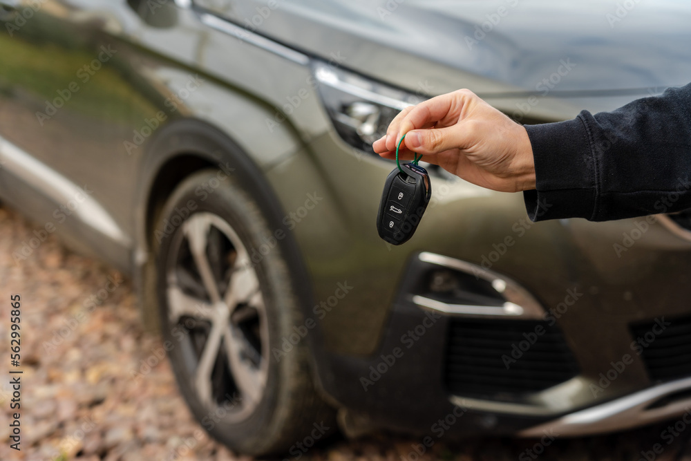 Person holding a car key in the hand stands front car. Insurance, loan and buying car concept