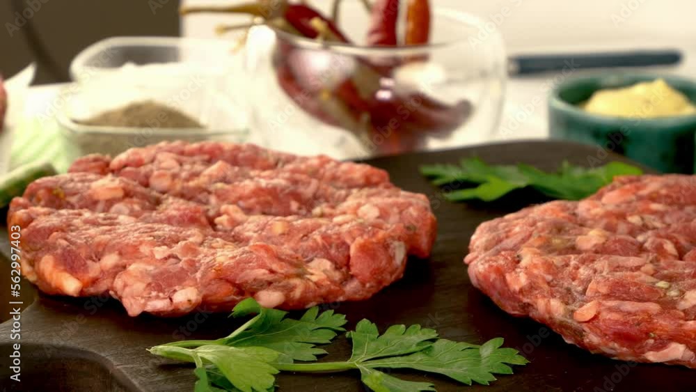 Round fresh raw mince beef burger cutlet with spices and sauce rotate on dark kitchen board. Round fresh raw mince beef burger cutlet with spices and sauce rotate on dark kitchen board.