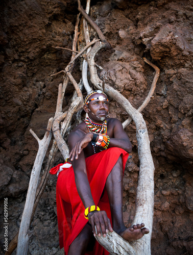 Portrait of a traditional Maasai guide standing on a makeshift wooden ladder.