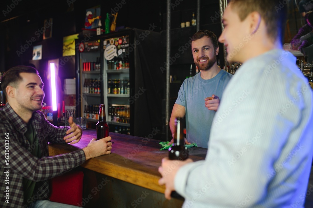 Obraz premium Two young men in casual clothes are smiling and talking while sitting at bar counter in pub