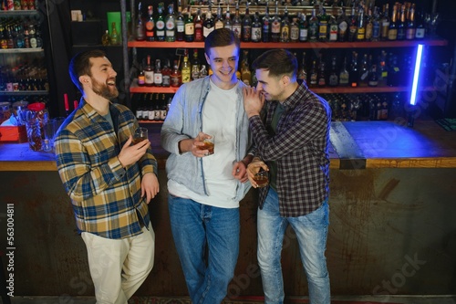 male friends spending time together in bar and having fun. Bearded men smiling, looking at each other and communicating. Men holding crystal glasses of whisky or scotch.
