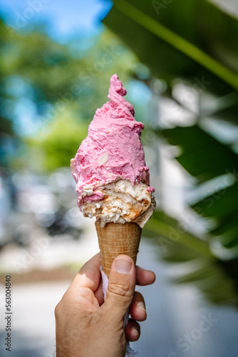 Ice cream in hand. Waffle cone with ice cream on the background of the street in the summer on a hot day. Street food, sweets, desserts concept. © uladzimirzuyeu