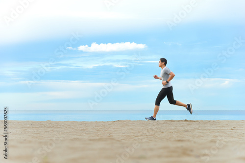 Asian man jogging on tropical sandy beach with blue sea and clear sky background.