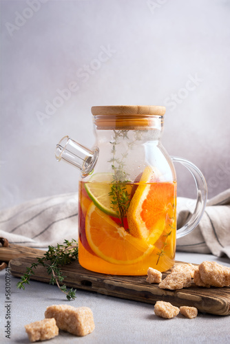 Glass teapot of hot healthy sweet fruit tea with fresh ripe citrus and thyme