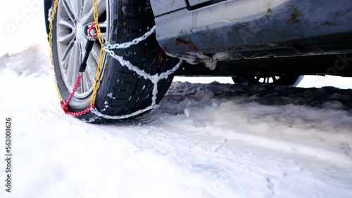 Snow chains on tire at winter road. Snow chains on the tire of a white car in winter on the snow. Winter bringing dangerous driving conditions for vehicles without snow chains.