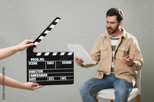 Obraz na płótnie Emotional actor performing while second assistant camera holding clapperboard on grey background, closeup