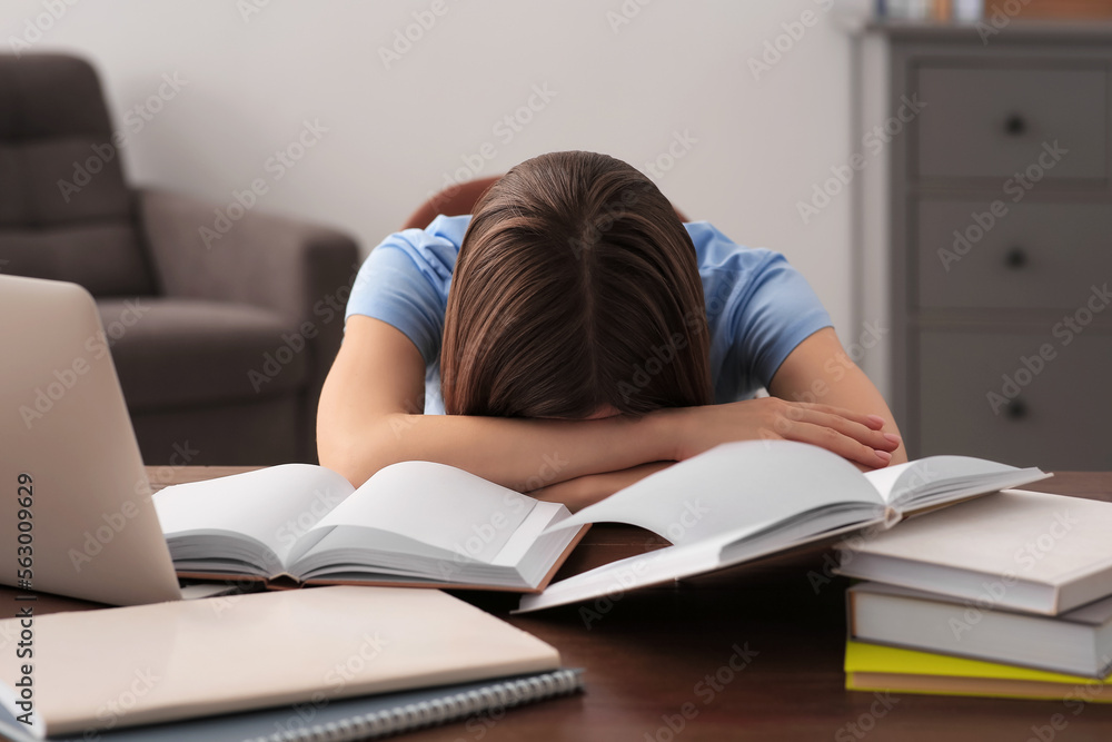 Young tired woman sleeping near books at wooden table indoors Young tired woman sleeping near books at wooden table indoors